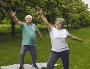Smiling elderly retired active couple exercising doing morning sports workout in park. Senior man and aged woman enjoy yoga or pilates physical training outdoors on fresh air. Healthy lifestyle